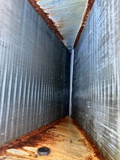 Rusty narrow metal corridor with corrugated walls and floor, viewed from one end.