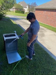 Person standing on grass using a hose to spray water into a metal box outdoors.