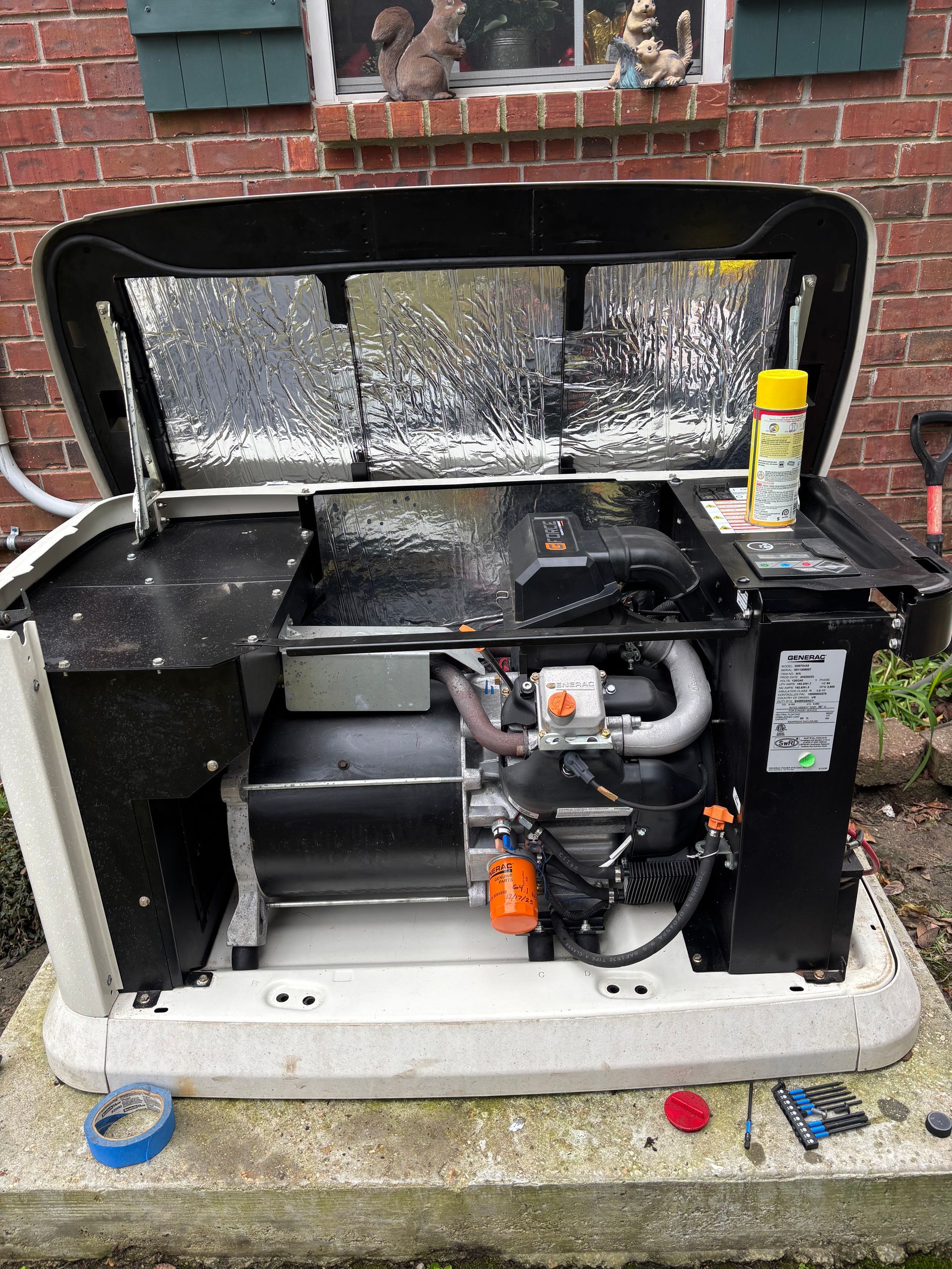 Open generator compartment with black and gray machinery, hoses, and a yellow can inside a brick-walled enclosure