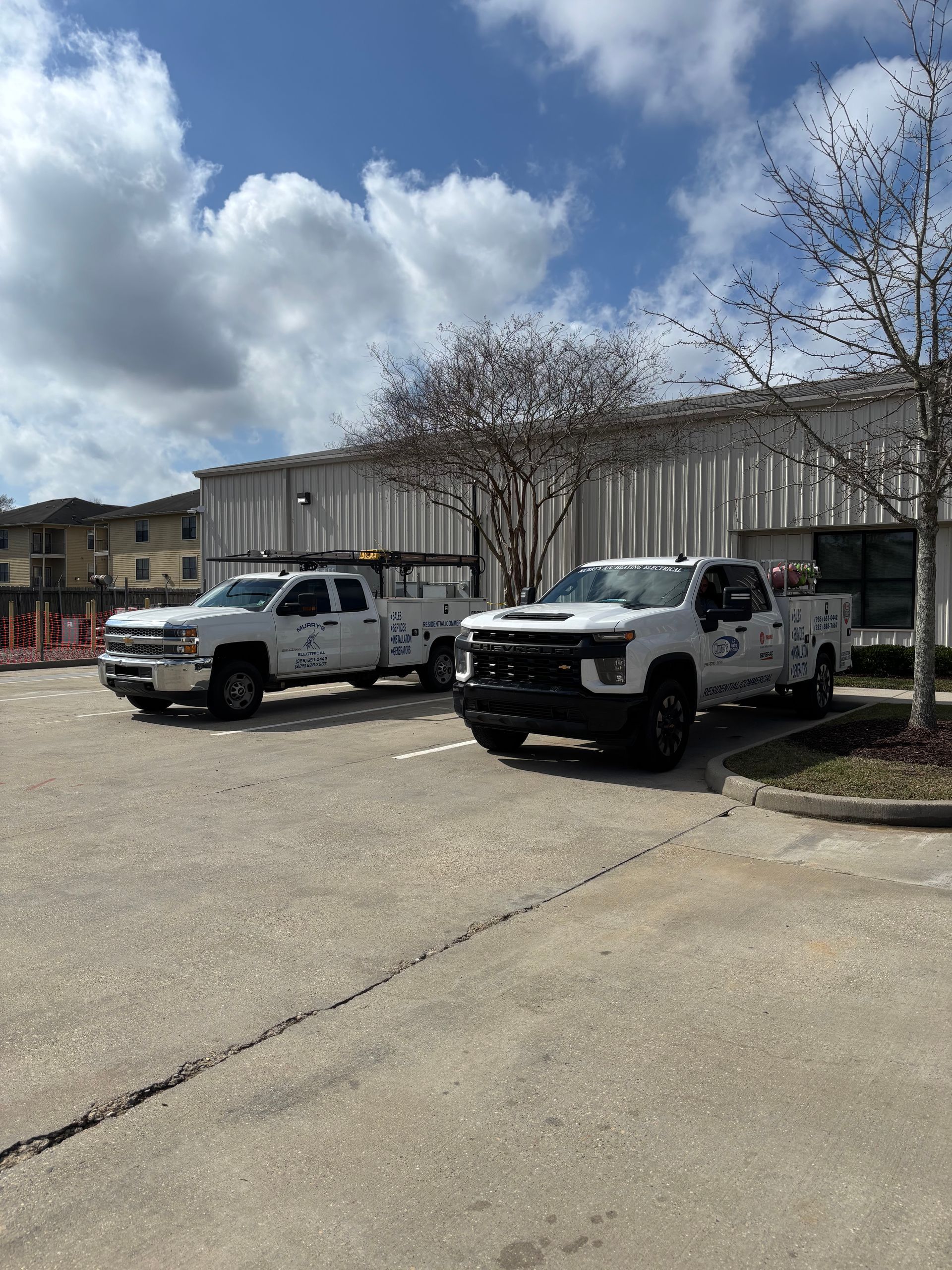 Two white utility trucks parked in front of a low building under a cloudy sky