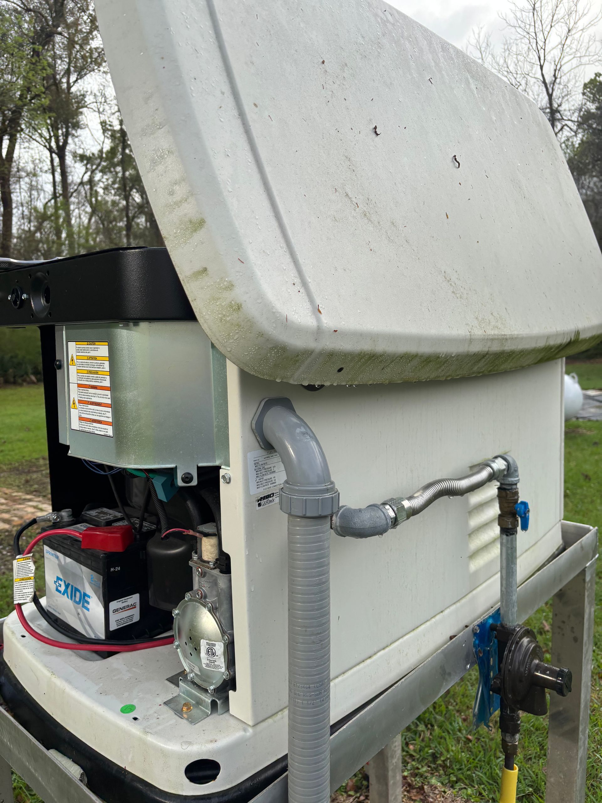 Outdoor utility equipment with a large white housing, pipes, and a battery unit in a wooded area