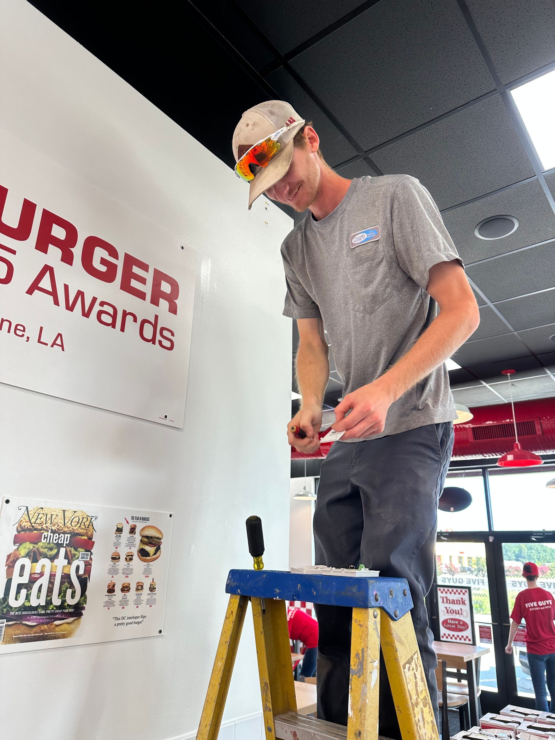 Man standing on a stool using a tool to work on a wall banner inside a store.