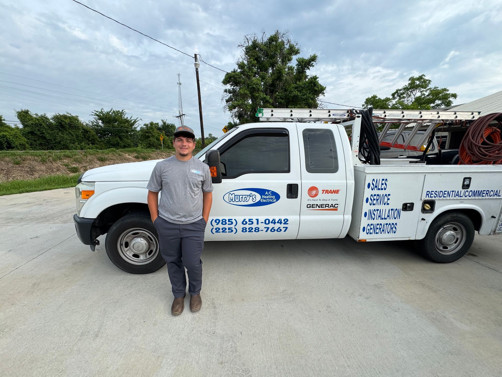 Man standing beside a white service truck on a gravel road under a cloudy sky