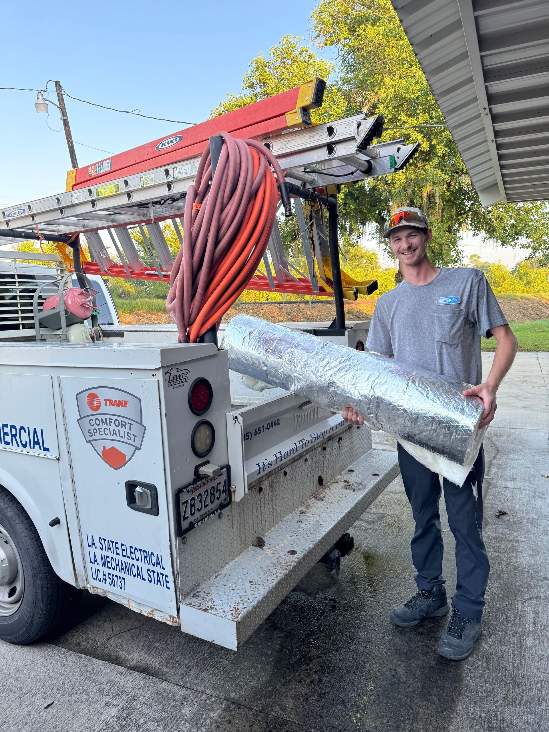 Worker standing beside a utility truck with ladder rack and coiled hoses on a wet street