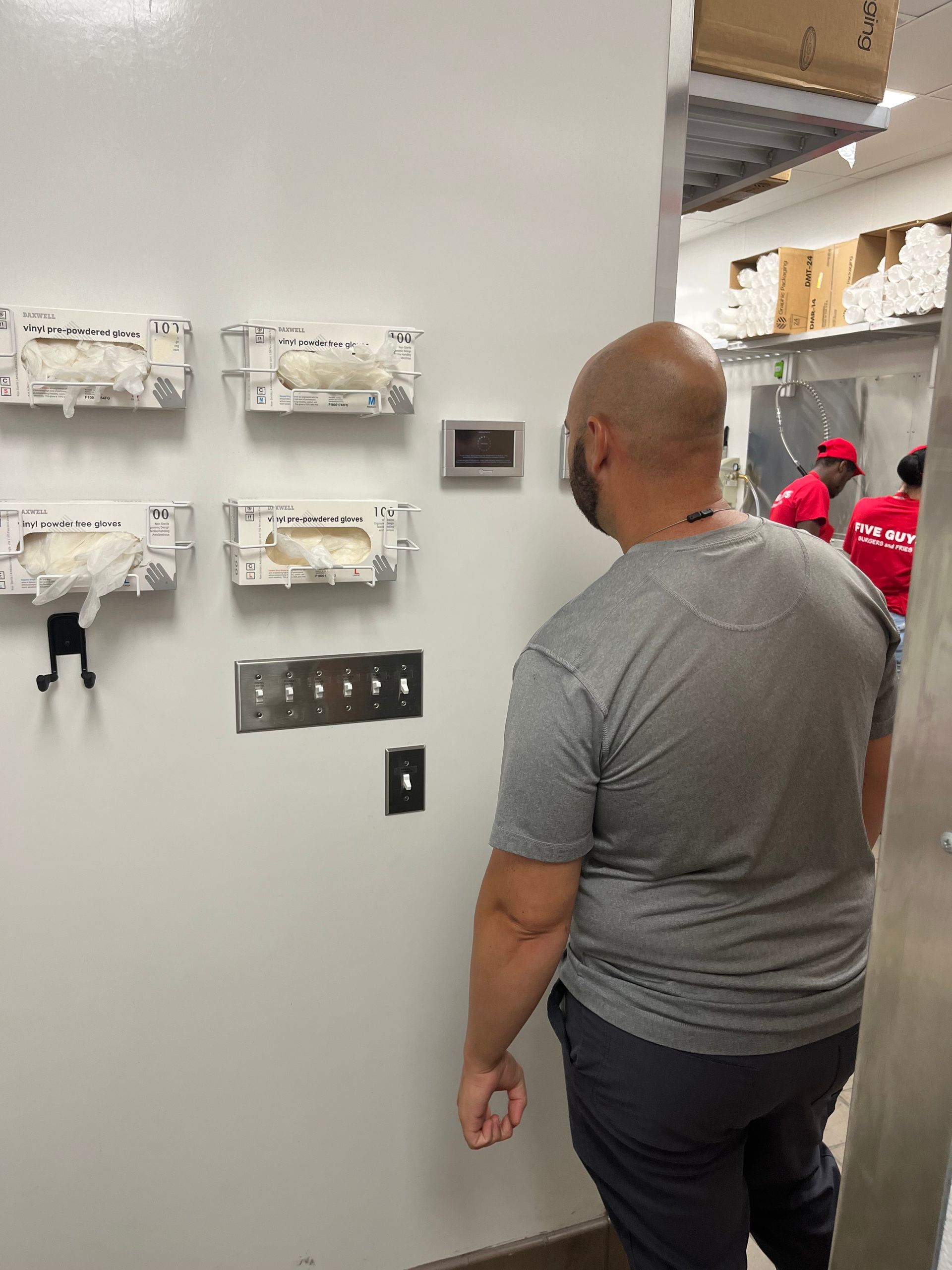 Person standing in a utility room looking at wall-mounted electrical panels and switches.