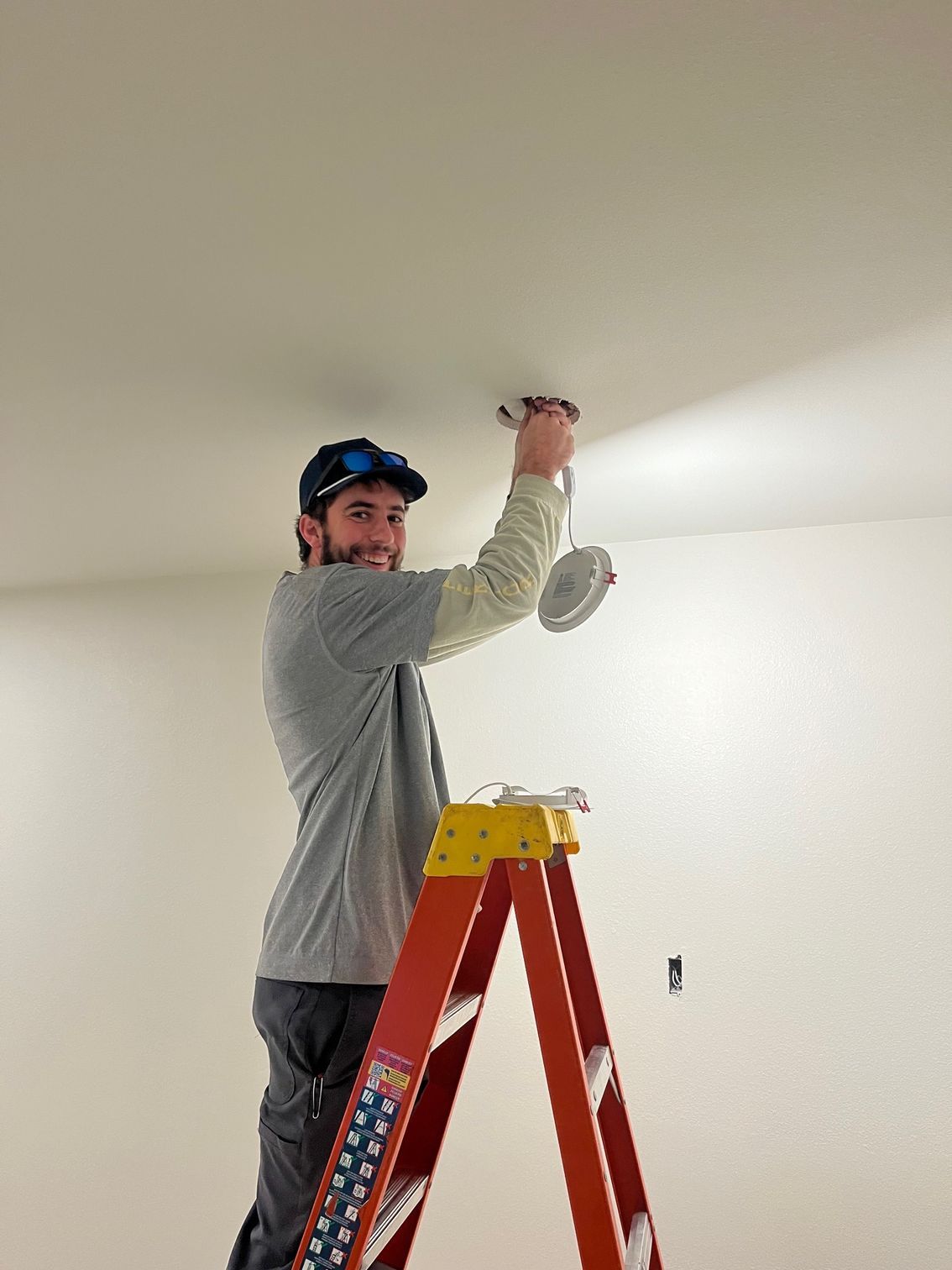 Person on a red ladder painting a white ceiling in a room with a roller.