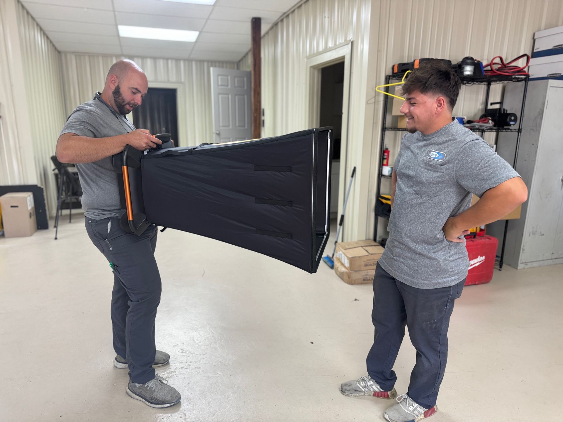 Two men in a workshop handling a large black folding partition