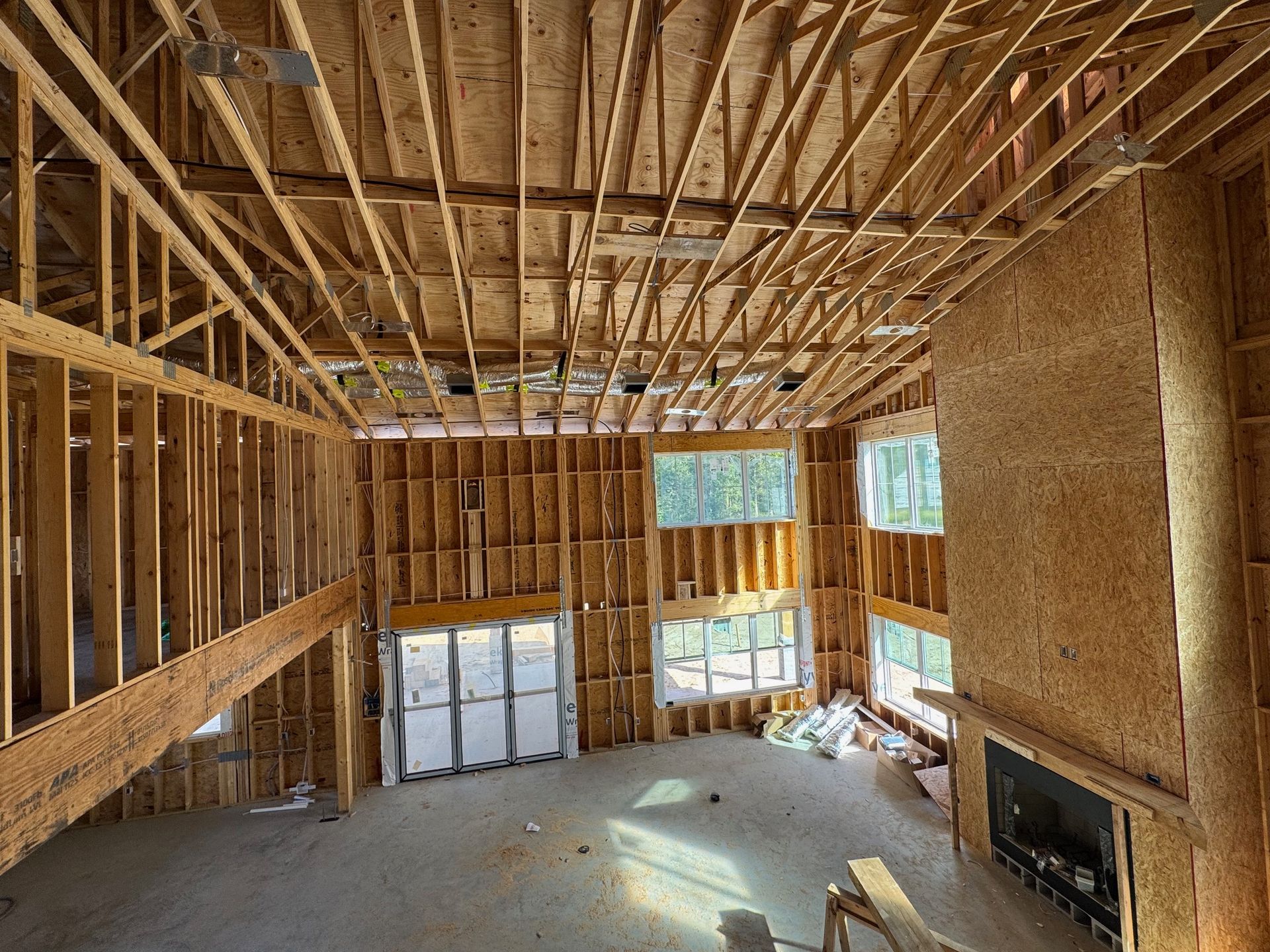 Unfinished house interior with exposed wood framing, tall windows, and a fireplace on the right.