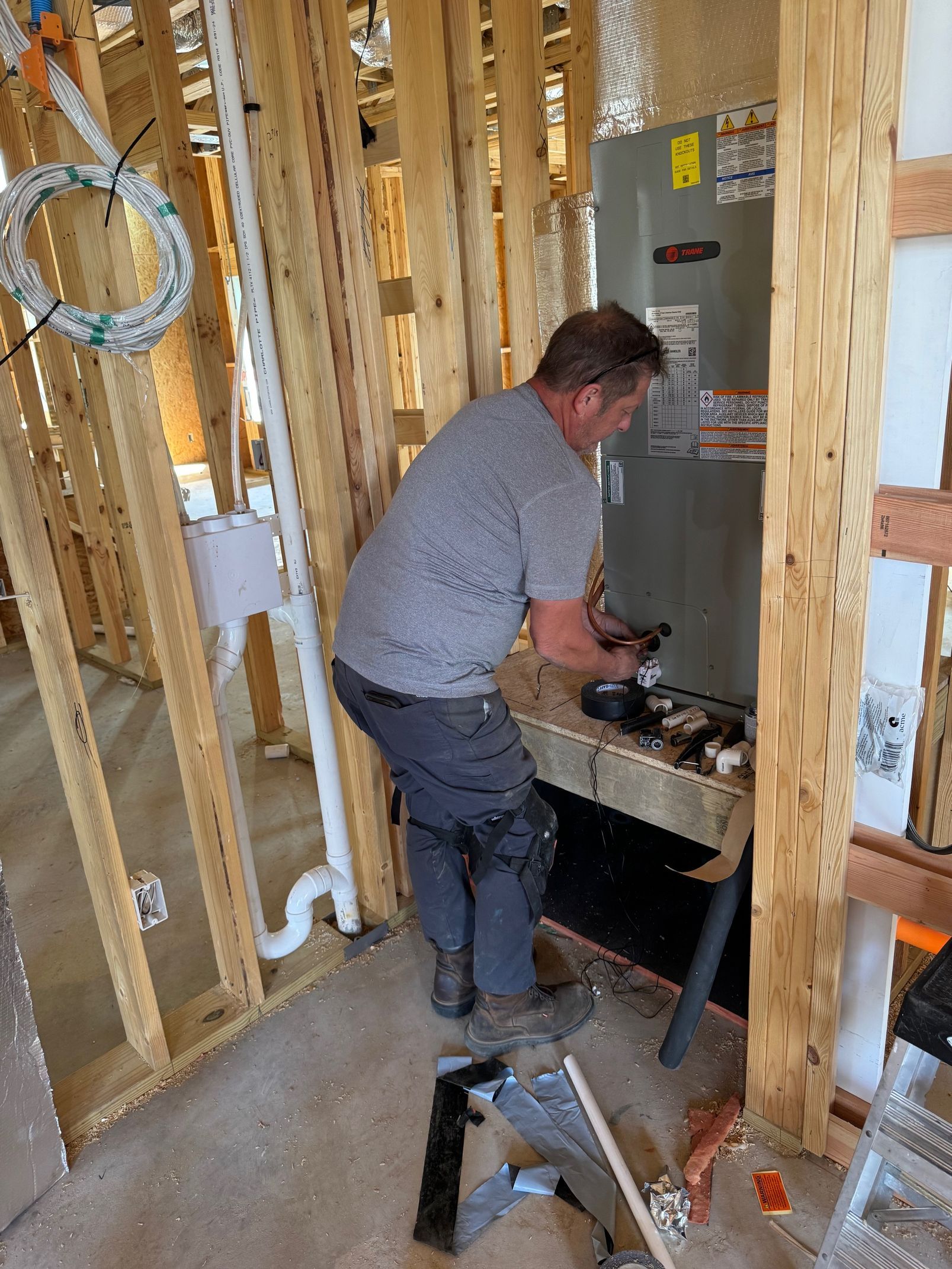 Man installing plumbing beside a furnace in a framed unfinished room