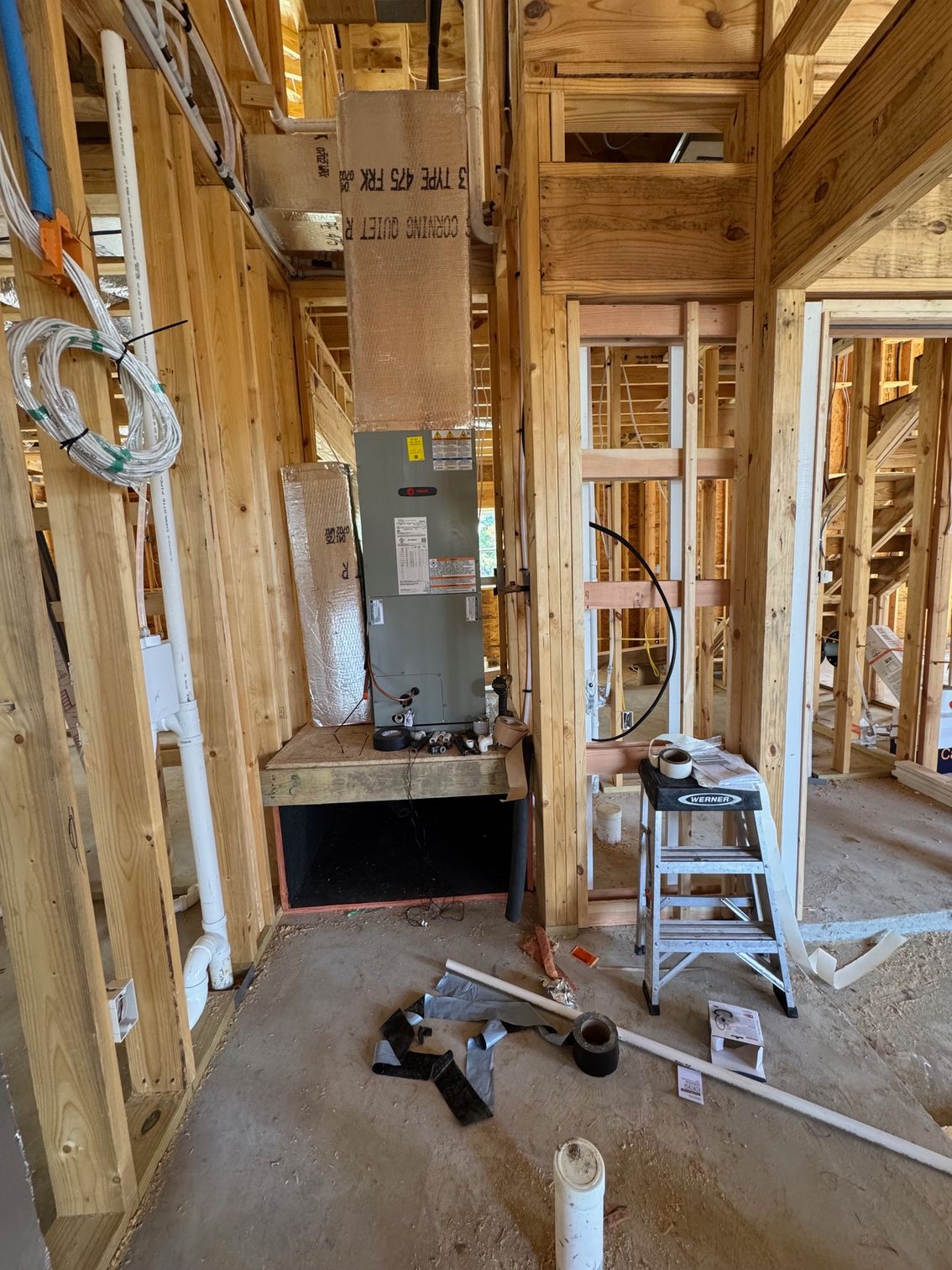 Framed house interior with electrical panel, exposed studs, and construction tools on the floor.