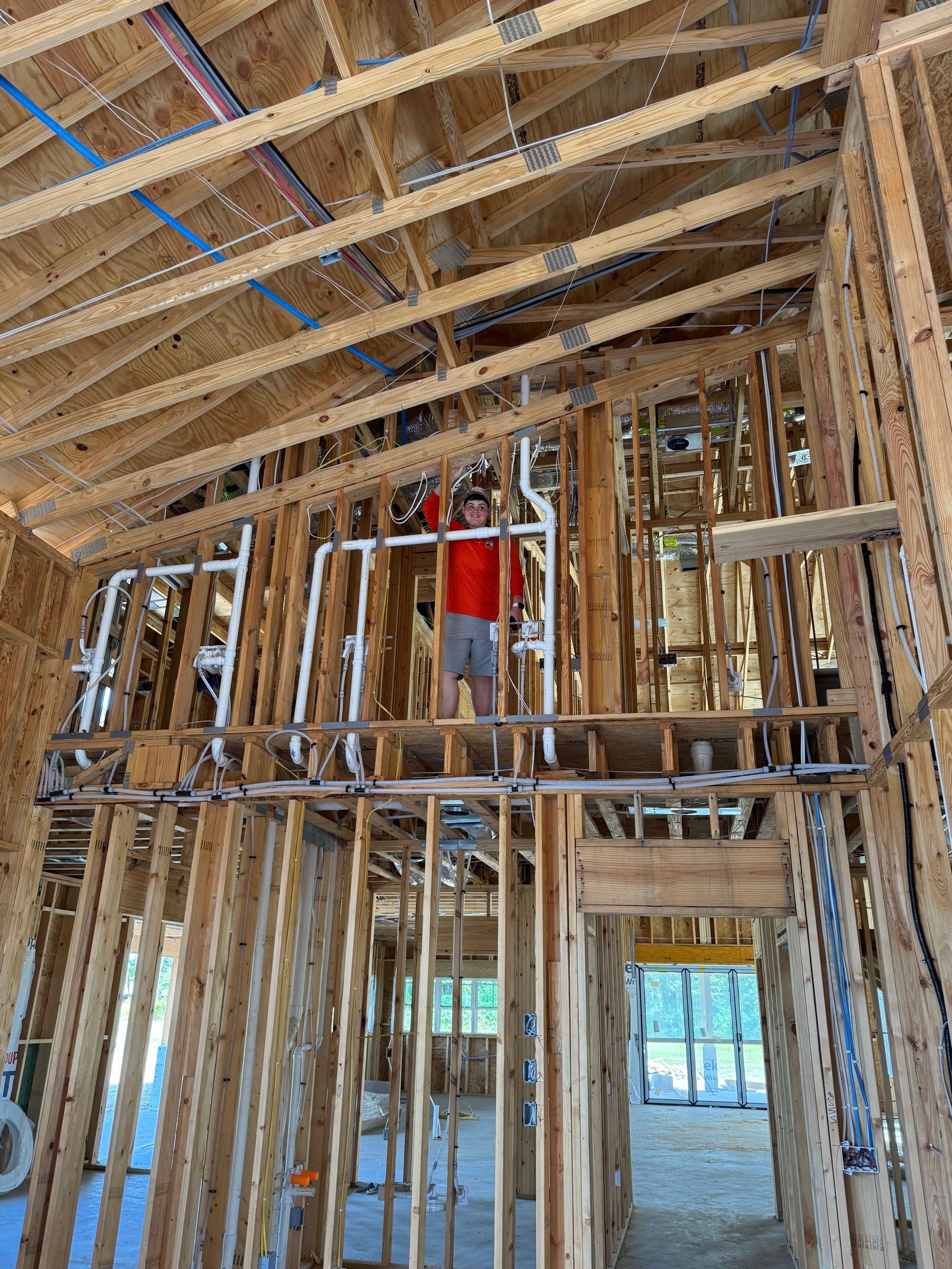 Interior of a house under construction with exposed wood framing and a worker in a red shirt on scaffolding