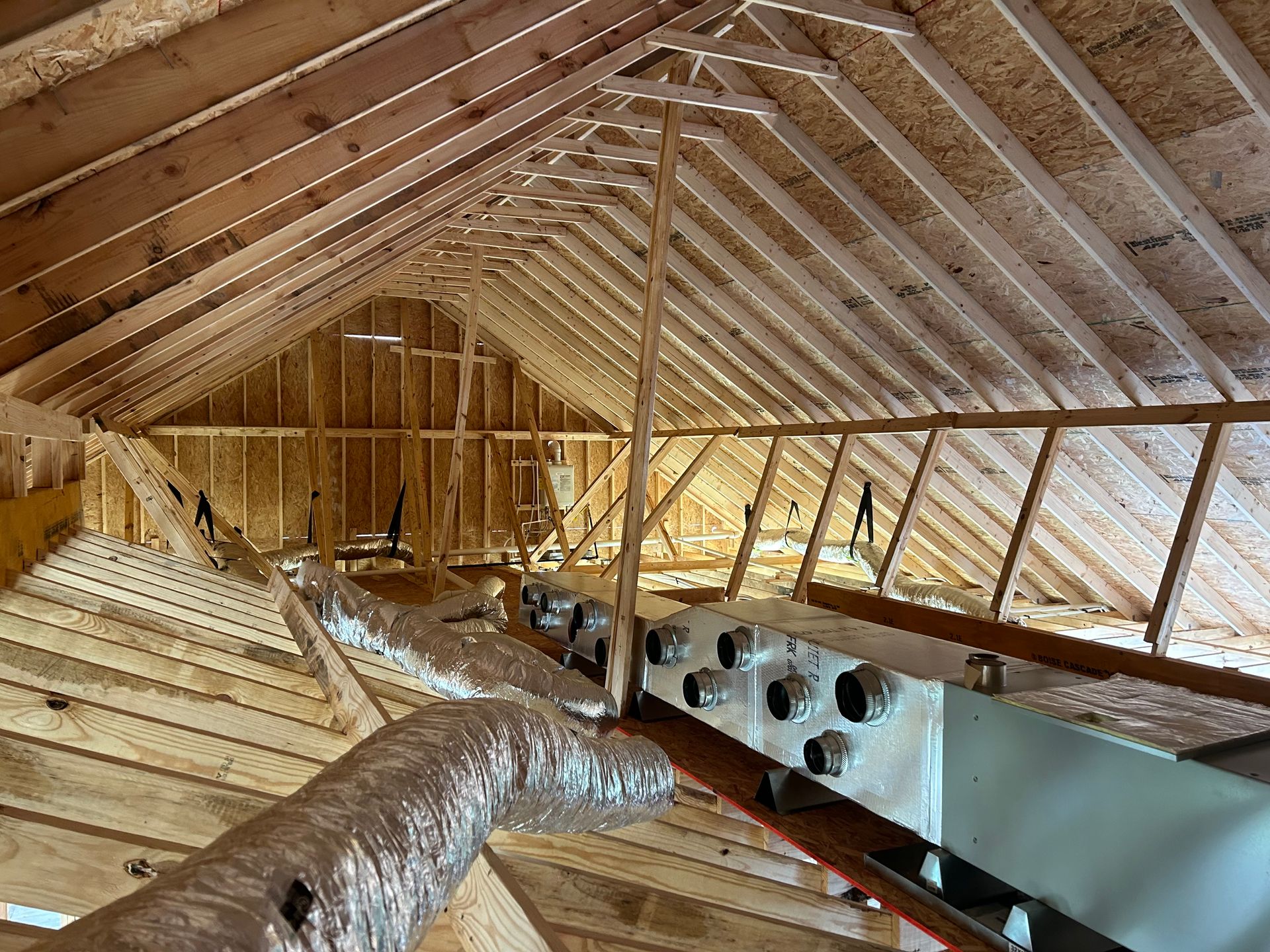 Partially insulated attic with exposed wooden rafters, ductwork, and daylight through the roof