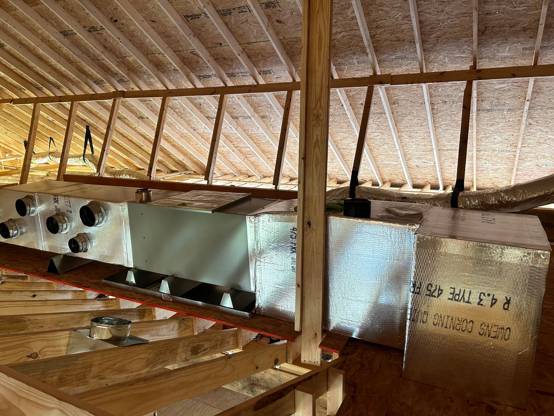 Interior of a rustic attic with exposed beams and a metal duct or panel along the wall.
