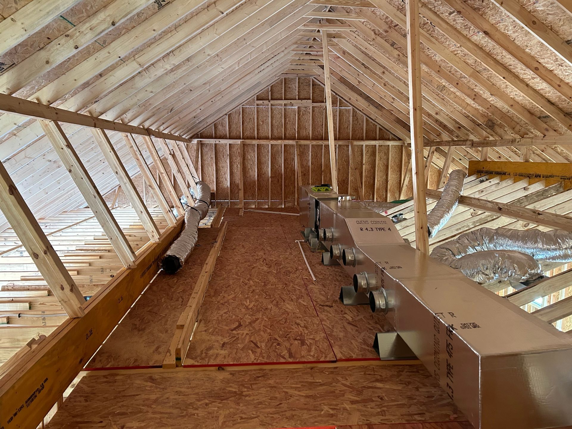 Attic interior with exposed rafters, insulation, and wooden floor framing under construction