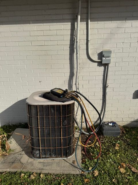 Outdoor air conditioner unit beside brick wall with electrical conduit and hoses attached