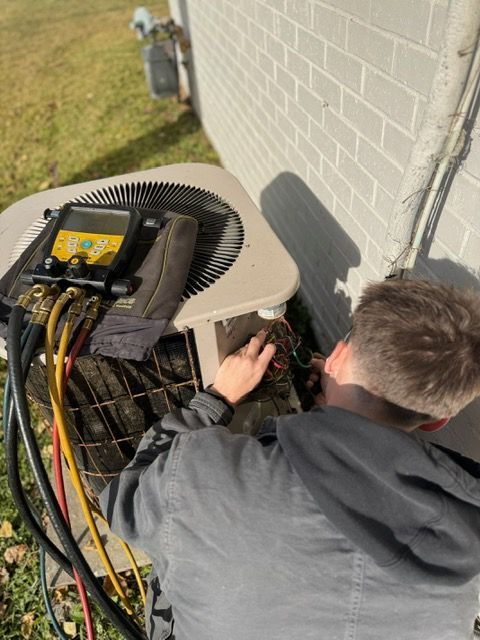 Technician working on outdoor HVAC unit beside a house wall, with tools and cables visible.
