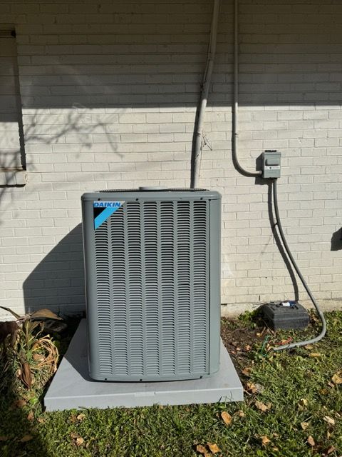 Outdoor HVAC unit beside a white brick house wall, with electrical conduit and a shrub nearby