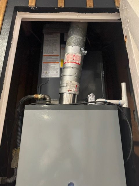 Gray HVAC furnace with metal ductwork in a wall opening above a black cabinet.
