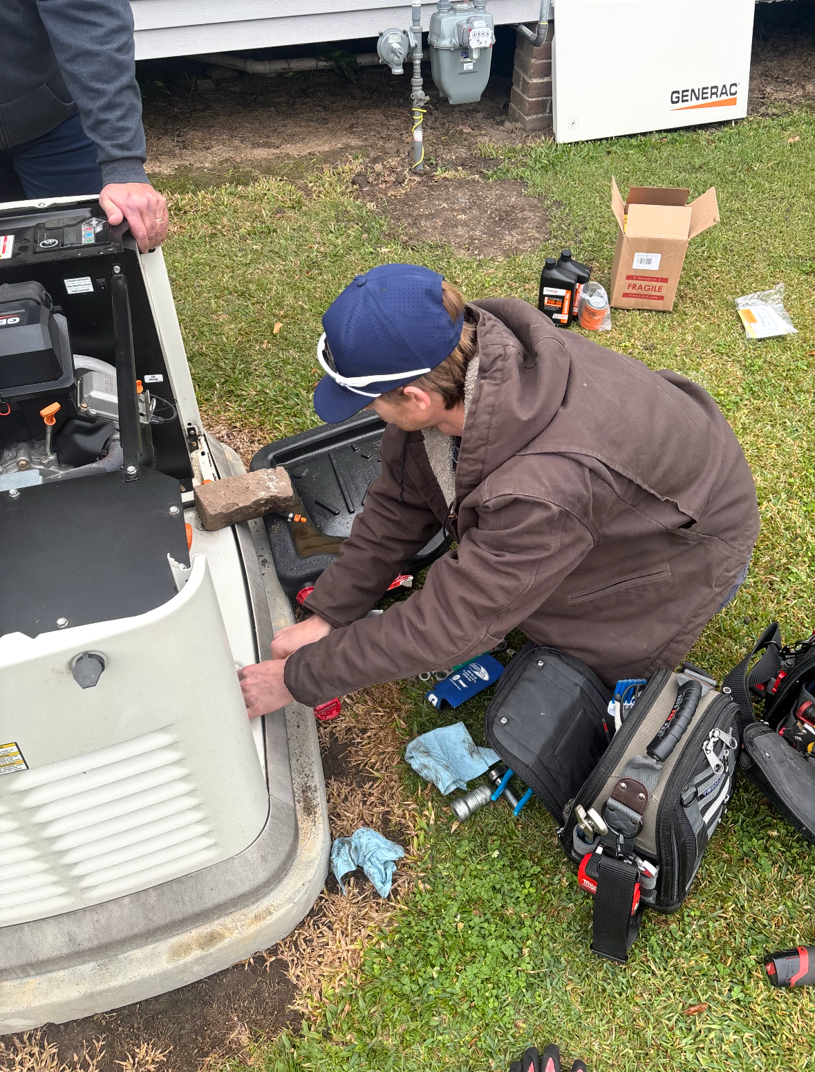 Person kneeling by an RV, using a tool to work on the vehicle’s front panel on grass.