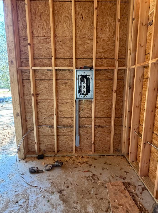 Interior wall framing with exposed electrical panel and OSB sheathing in an unfinished room