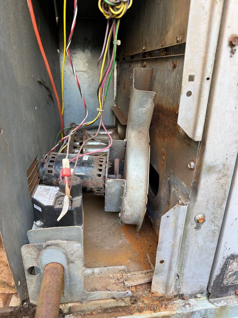 Open electrical/mechanical compartment with wires, motor, ducts, and rusted metal parts on the floor.