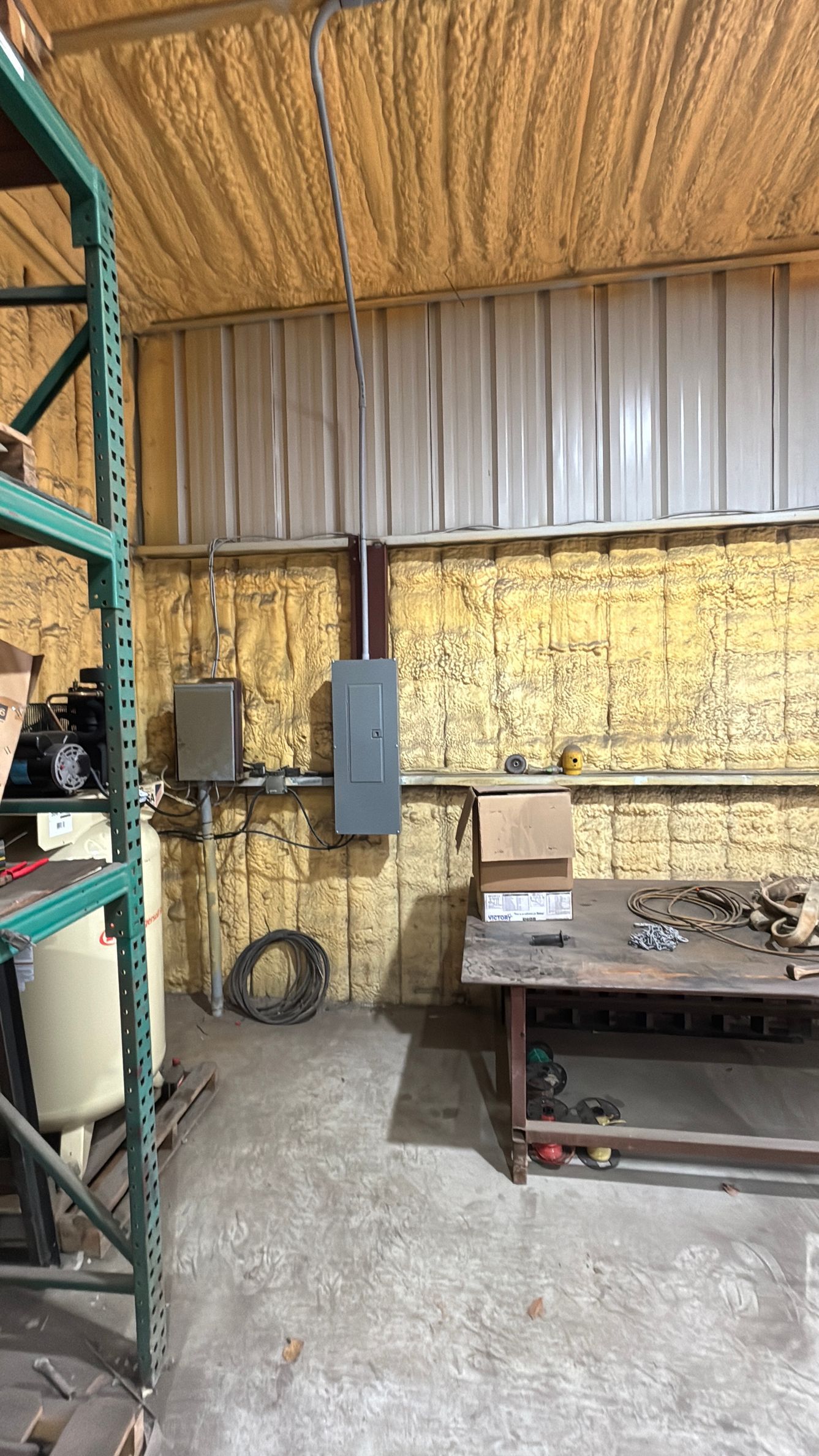 Industrial workshop interior with metal shelving, electrical boxes, and a workbench against insulated walls