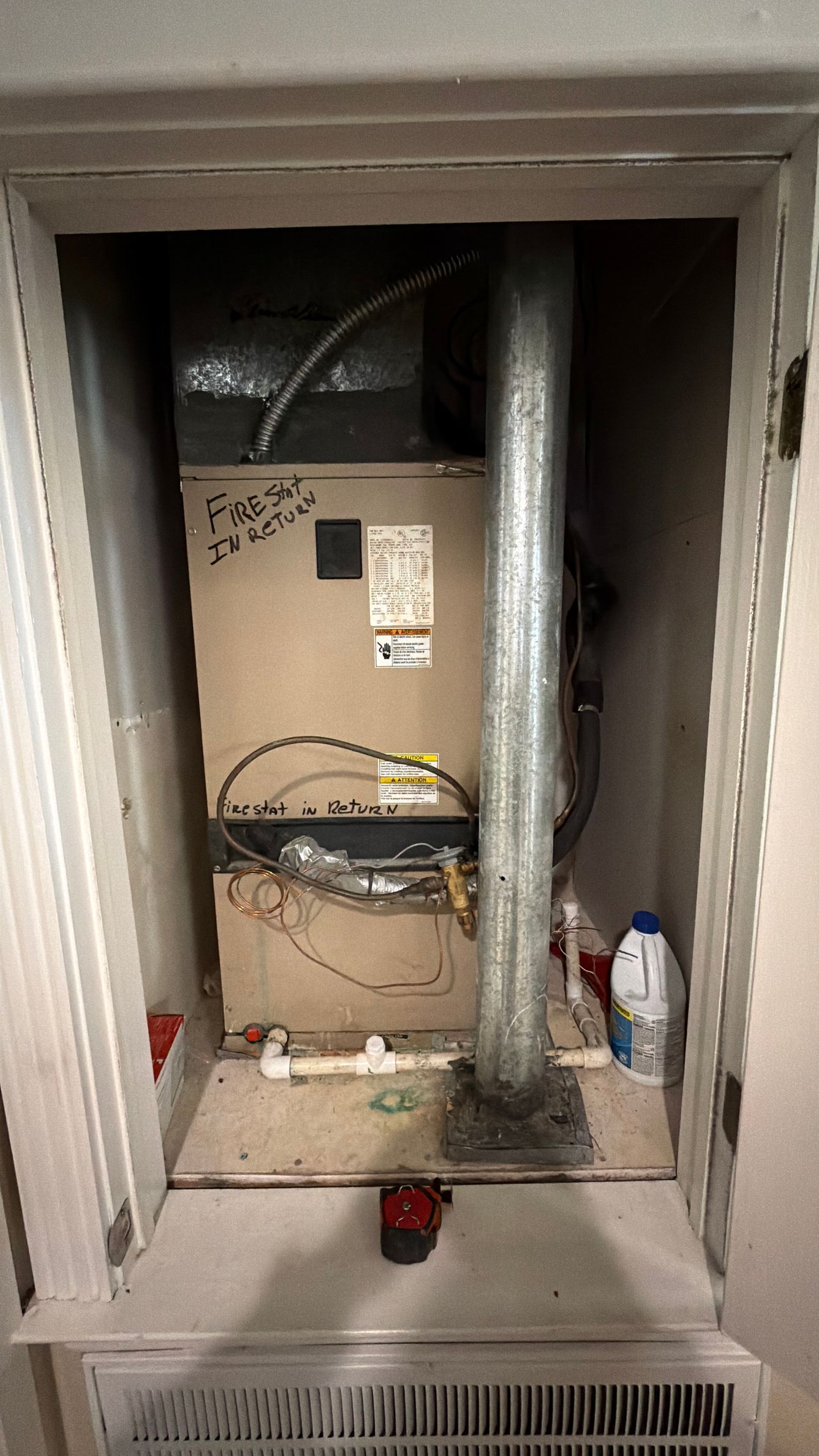 Open utility closet with HVAC unit, ductwork, and cleaning supplies in a beige cabinet.
