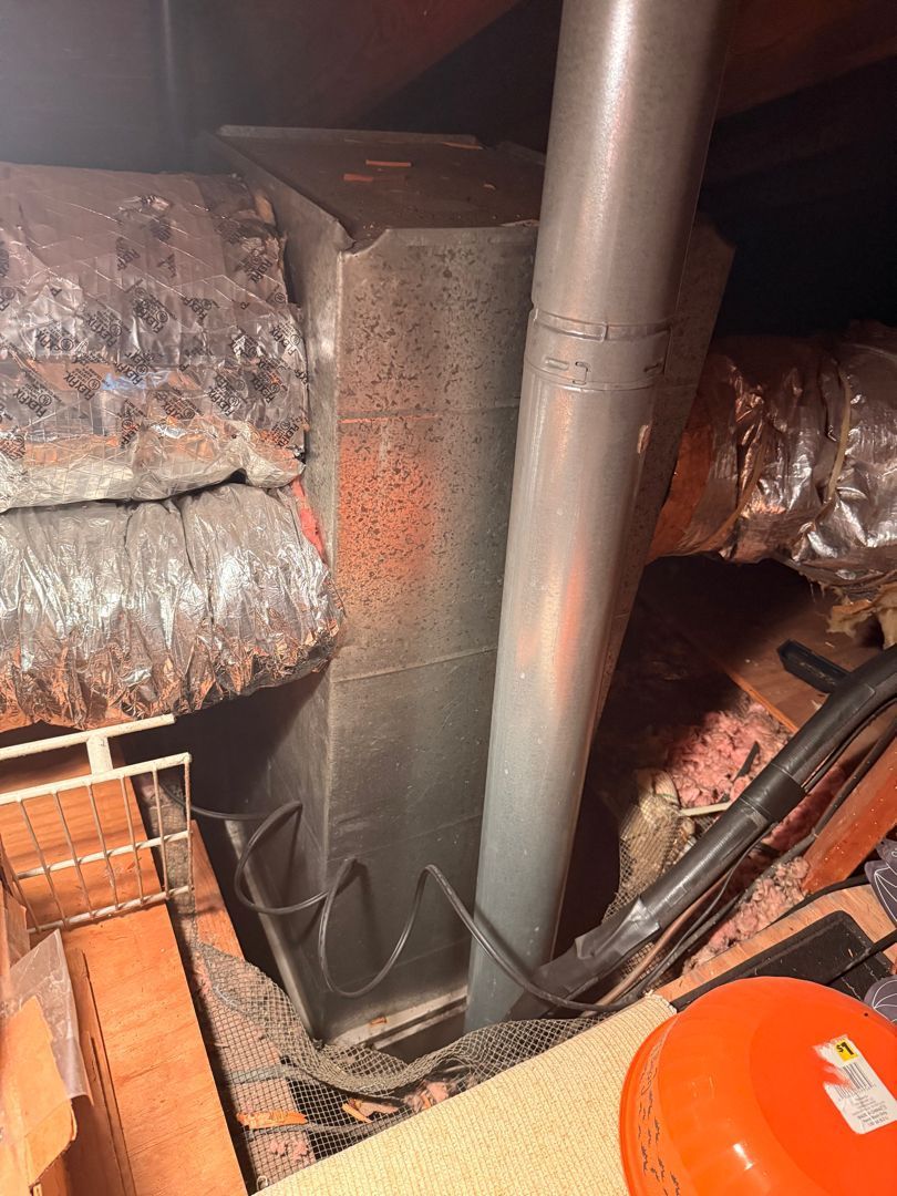 Dim attic with insulated ducts, a central metal pipe, and exposed wiring near the floor opening