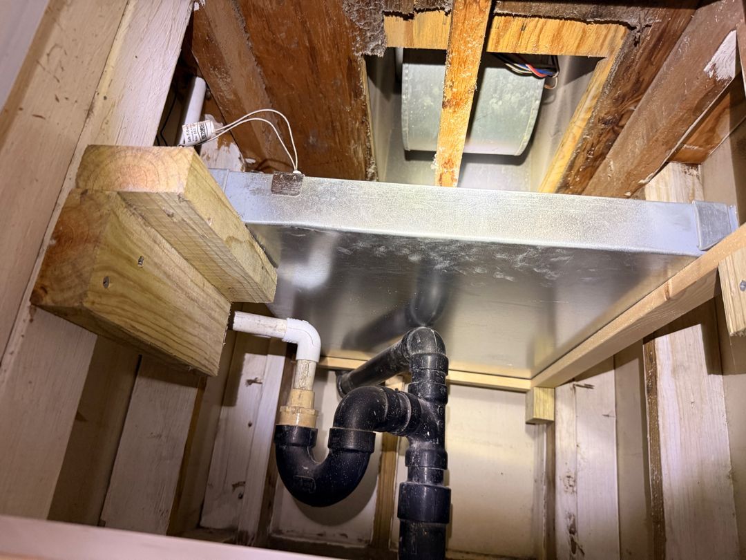 Open ceiling showing exposed wooden joists and black PVC plumbing pipes under a floor.