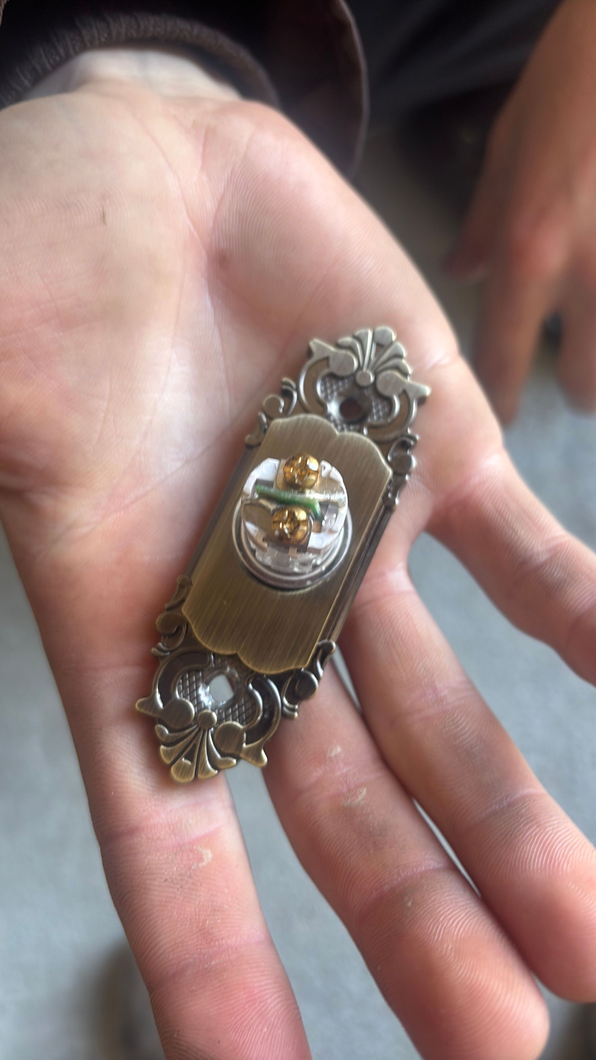 Small ornate vintage brooch with a central clear gem resting in a person's open palm.