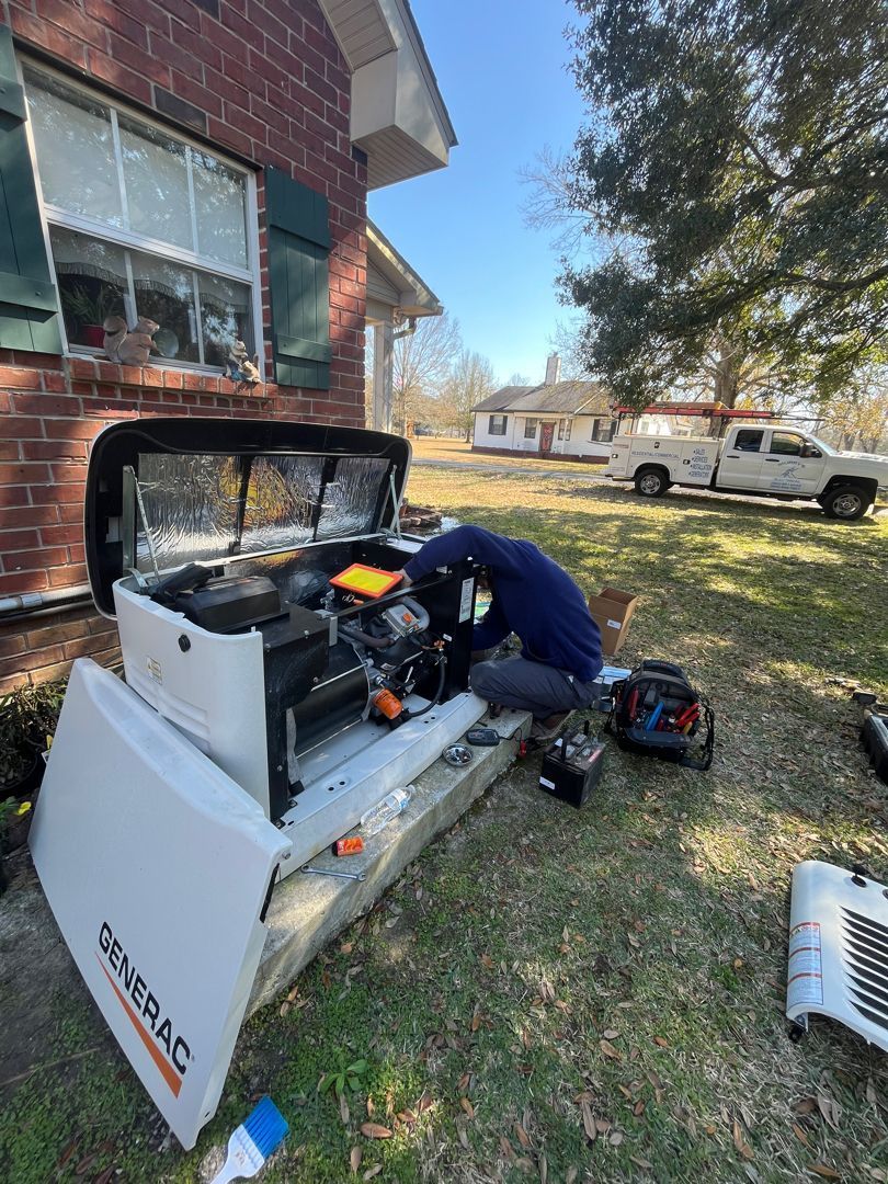Worker repairing HVAC unit beside brick house, with tools and open equipment case on the lawn.