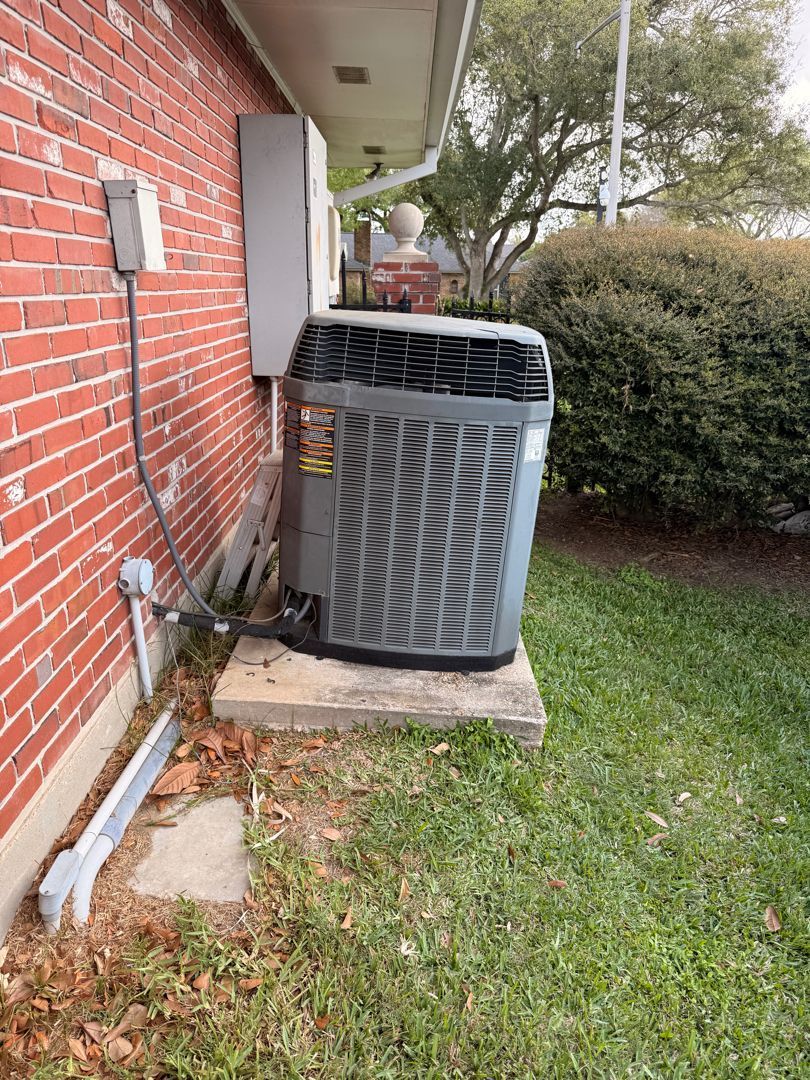 Outdoor HVAC unit beside a brick house, near a hedge and grass lawn