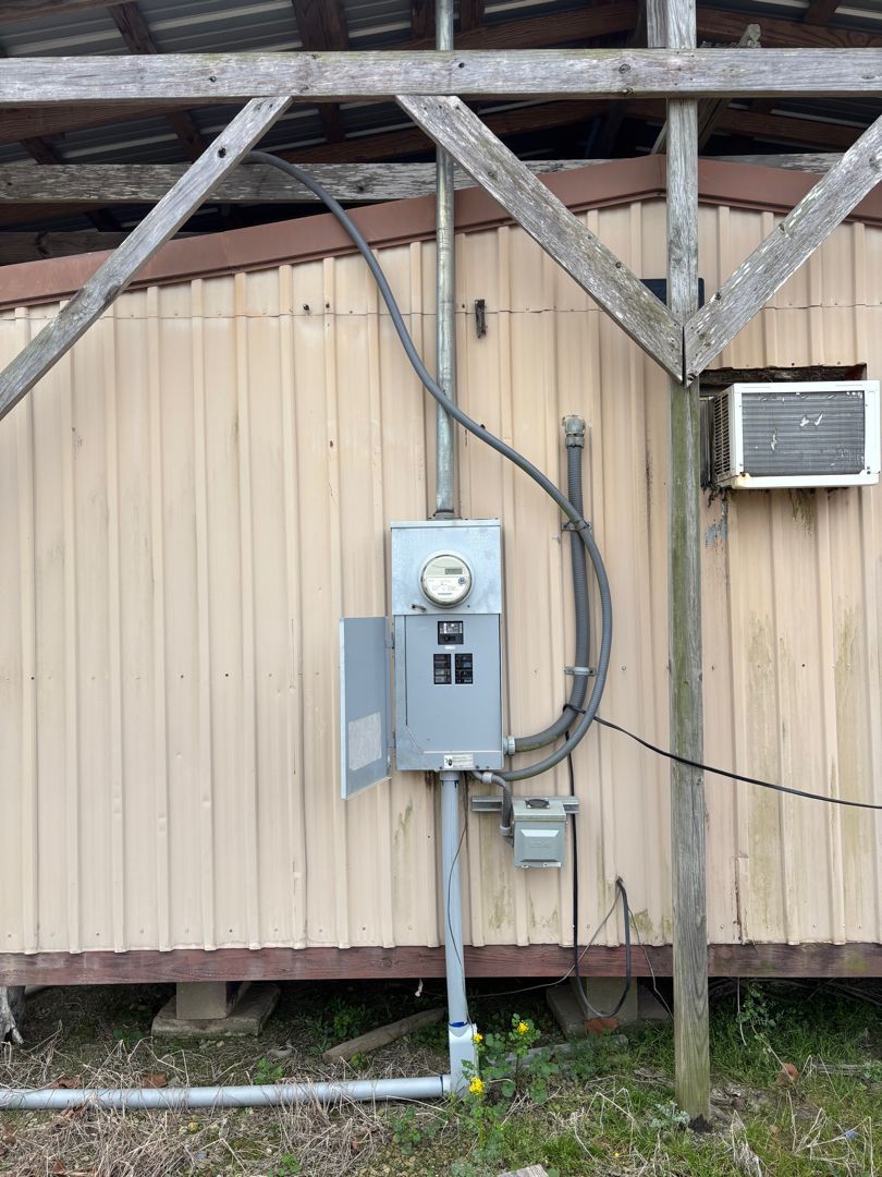 Electric meter and service box mounted on a beige exterior wall under wooden roof supports.