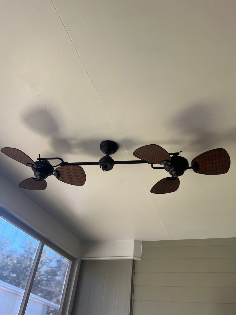 Ceiling fan with brown leaf-shaped blades mounted in a room with a window and wall paneling
