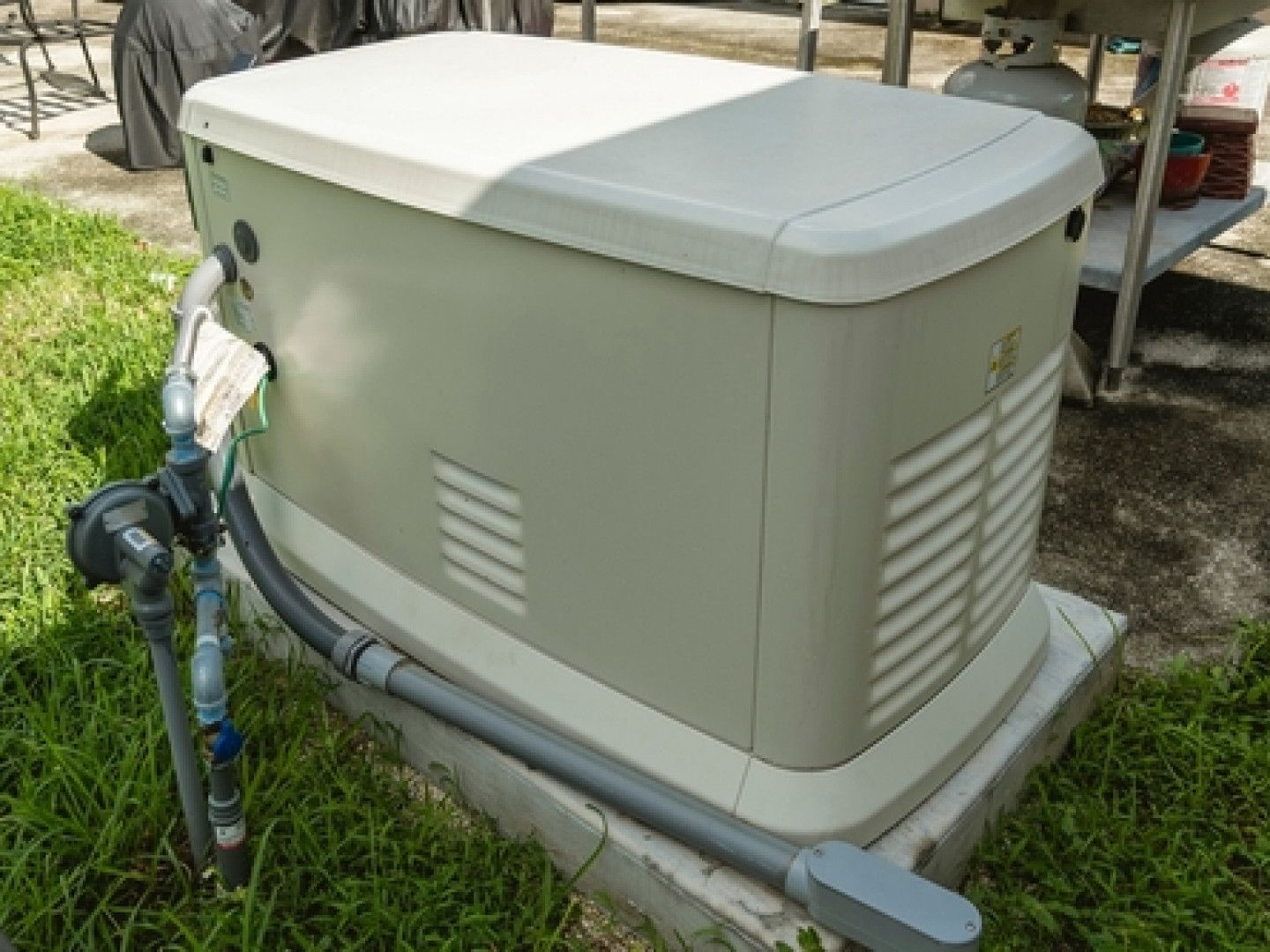 Gray outdoor generator on a concrete pad with pipes and valves beside a house-style structure