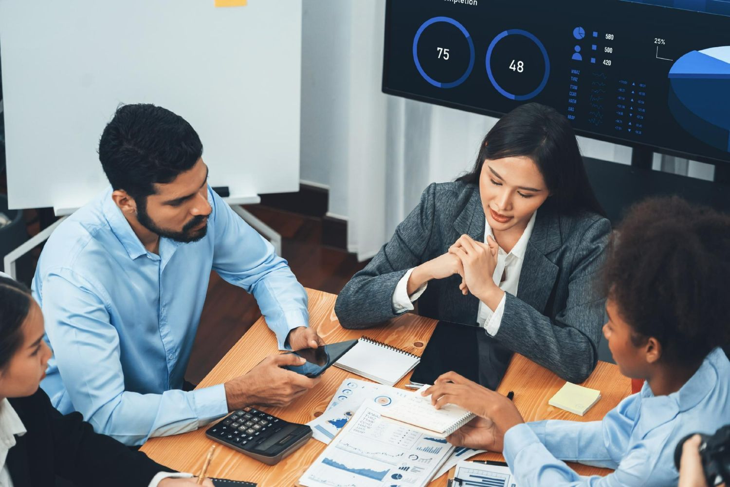 A diverse professional team in a modern office reviews financial data and charts together at a table.