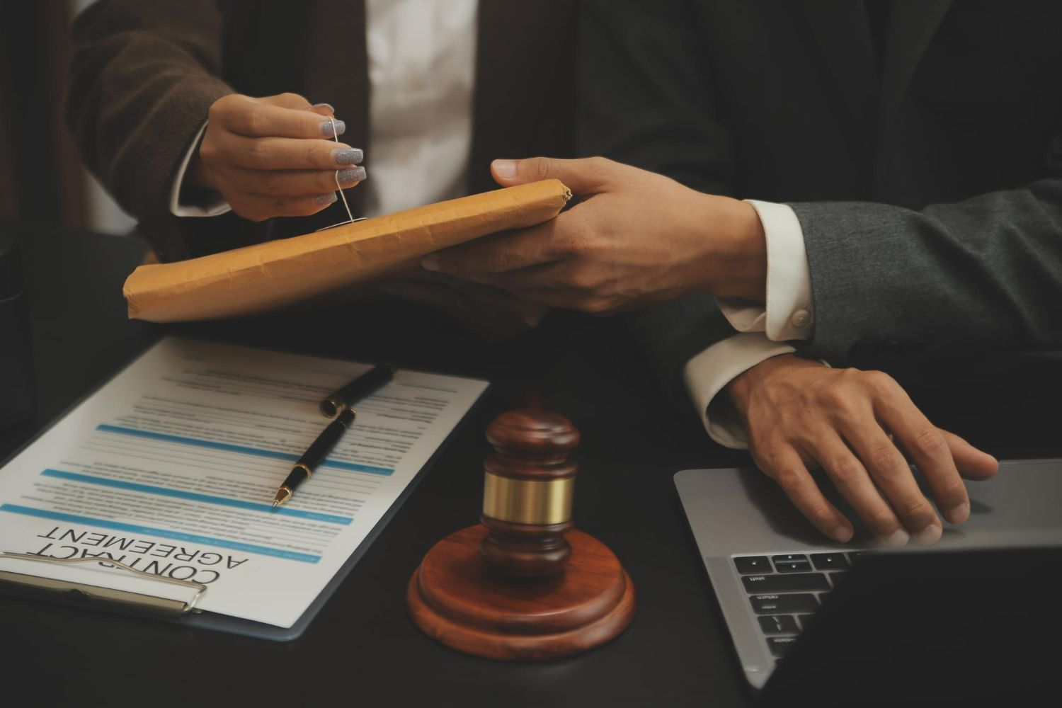 Two business professionals reviewing documents and a contract agreement on a table with a wooden gavel.