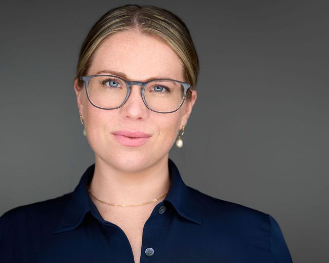 A woman wearing glasses and a blue shirt is smiling for the camera.
