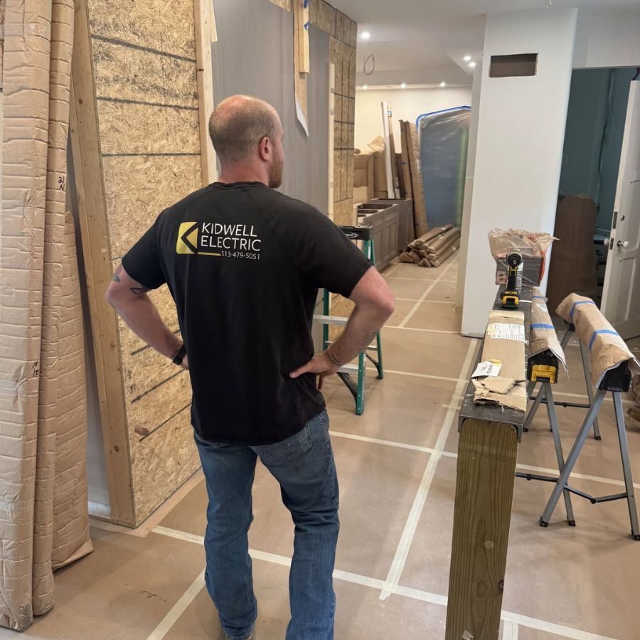 Worker in a hallway under renovation, with taped floor markings and construction materials on both sides.