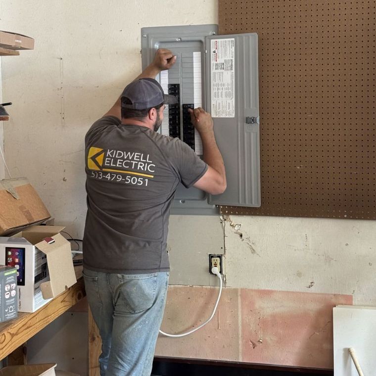Electrician installing wiring in an open breaker panel inside a workshop.