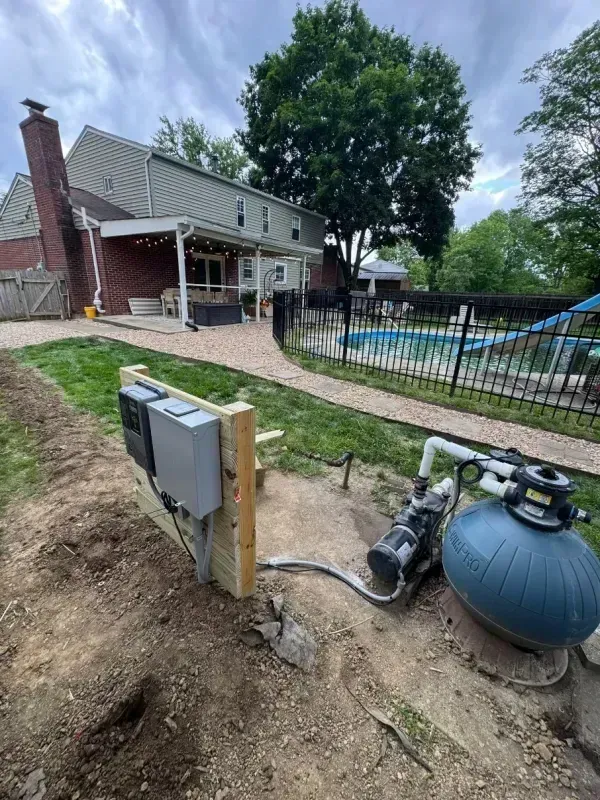 Backyard with pool equipment, utility boxes, and a brick house under cloudy skies