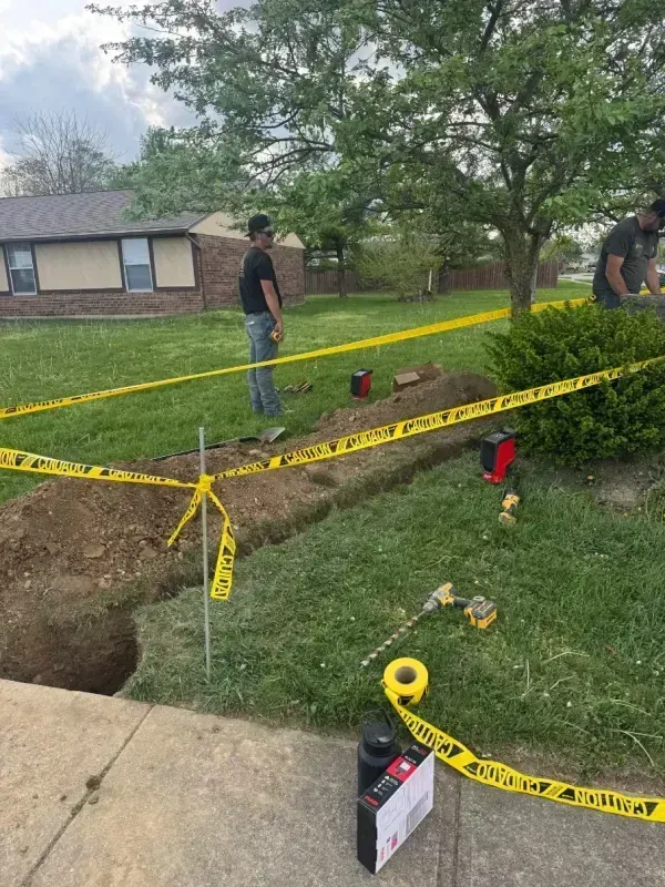 Utility crew inspecting a yard trench marked with yellow caution tape and tools near a house