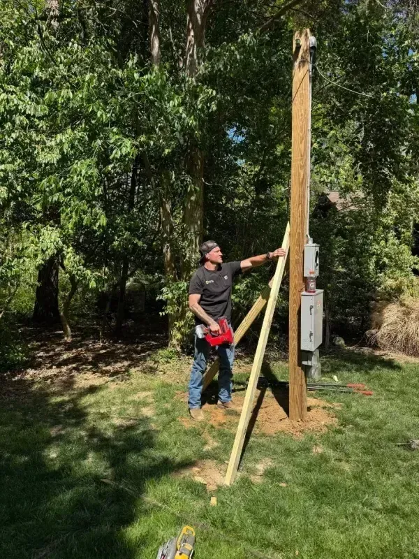 Person measuring a tall wooden post with a tape measure in a grassy wooded area