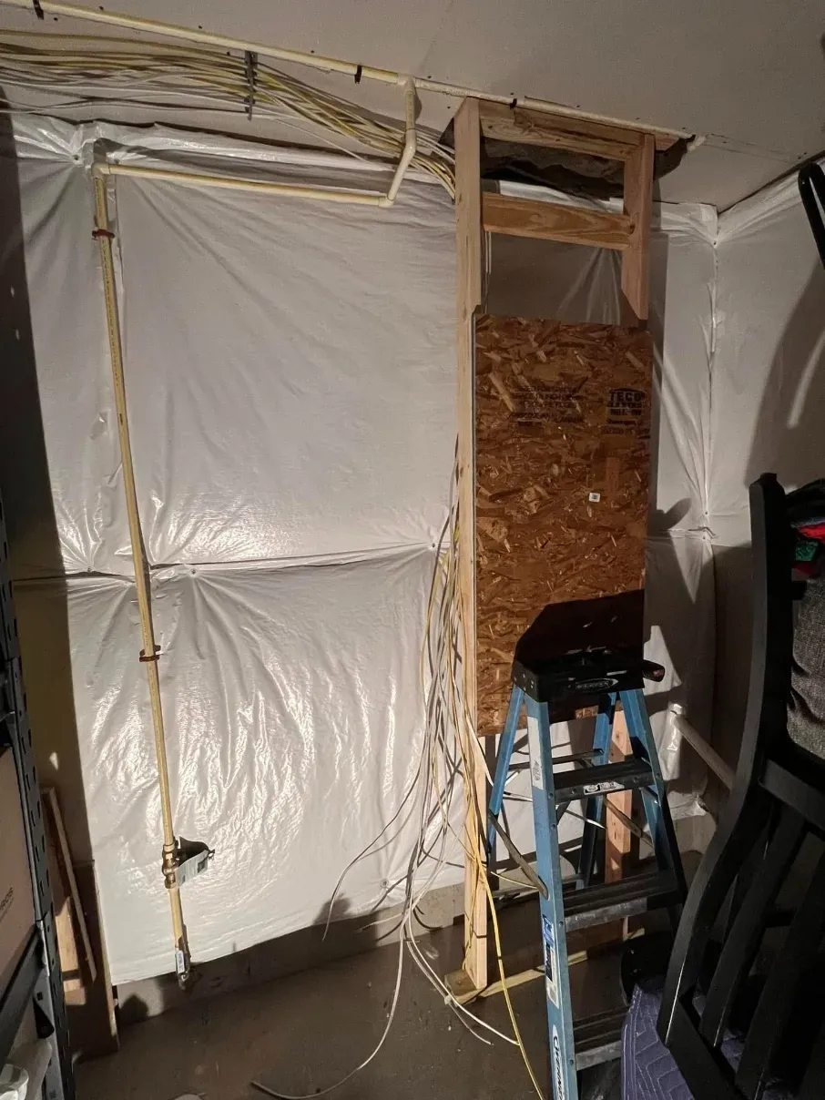 Makeshift wall repair with white plastic sheeting, exposed insulation, and a step ladder indoors