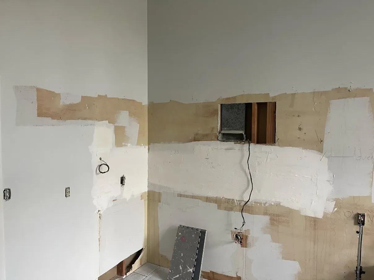 Partially renovated room with patched white walls, exposed wiring, and a small wall opening