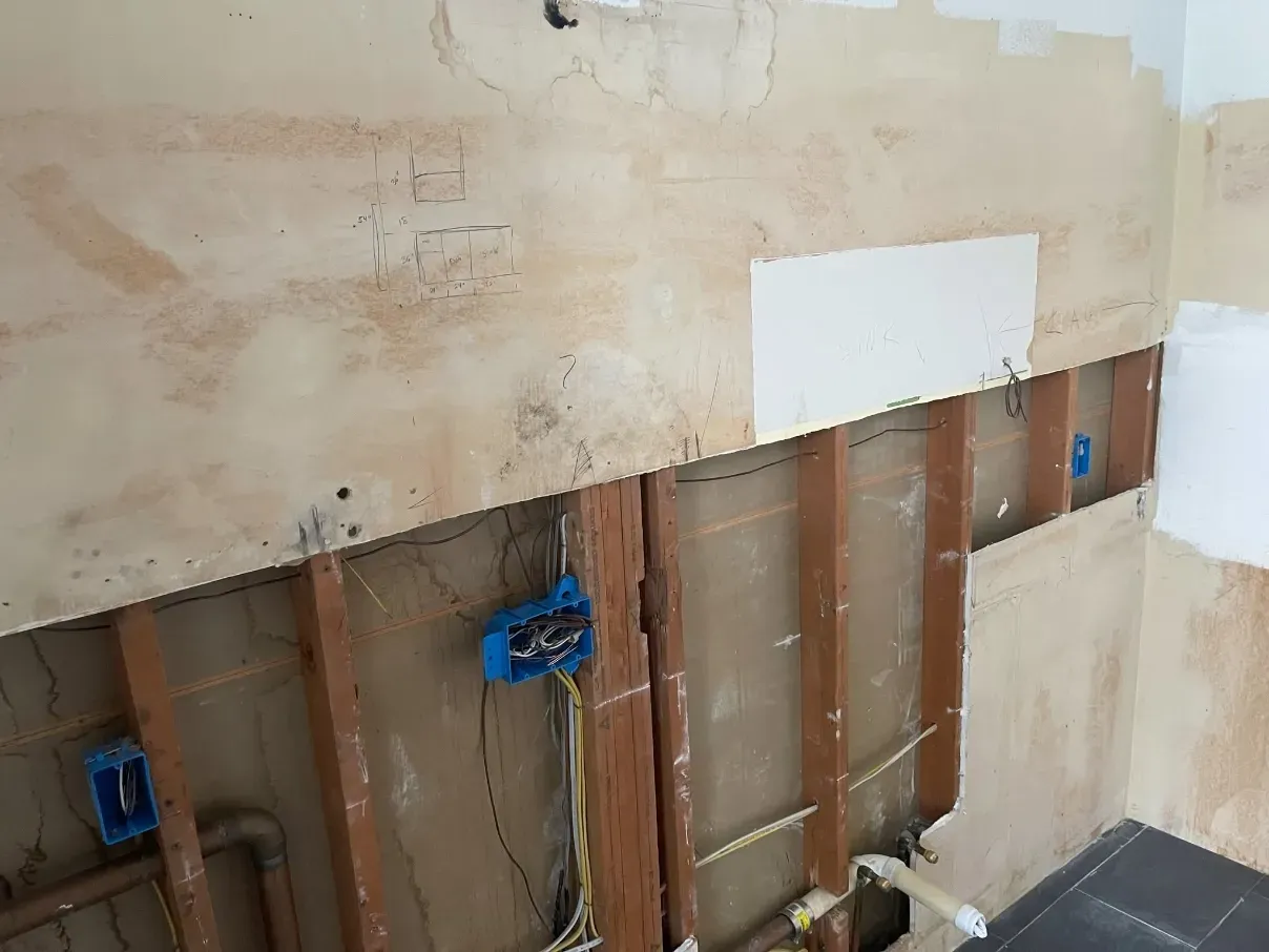 Damaged interior wall with exposed studs, wiring, and plumbing during renovation