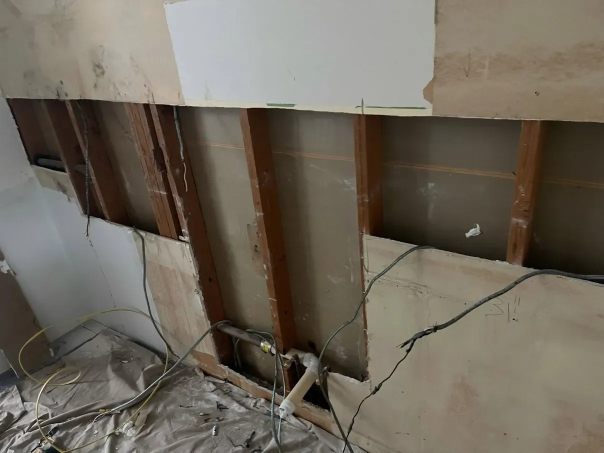 Exposed wall studs and damaged drywall in a room under renovation, with debris on the floor.