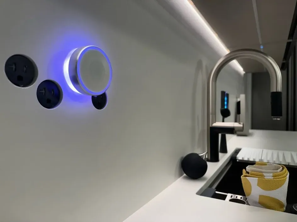 Modern RV interior with white walls, blue-lit control dial, archway, and a cup on the countertop