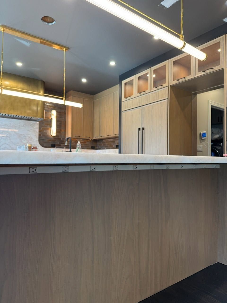 Modern kitchen with wood cabinets, marble island, and pendant lights under a dark ceiling.