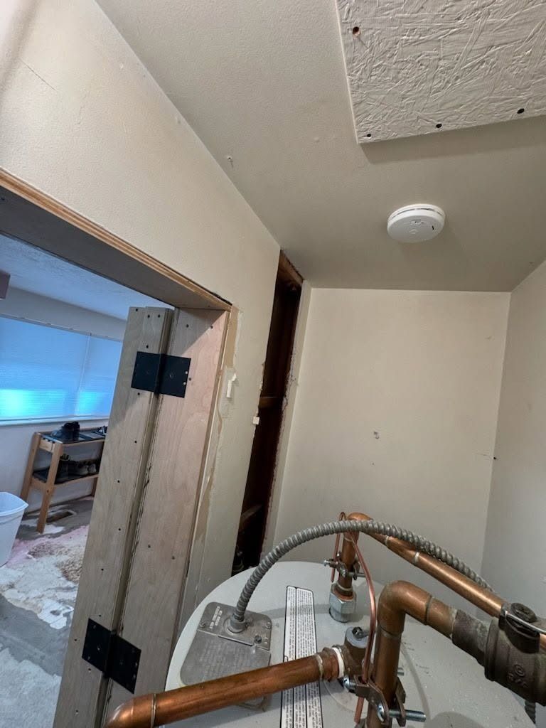 Interior hallway with exposed copper pipes and a doorway opening into a room under renovation